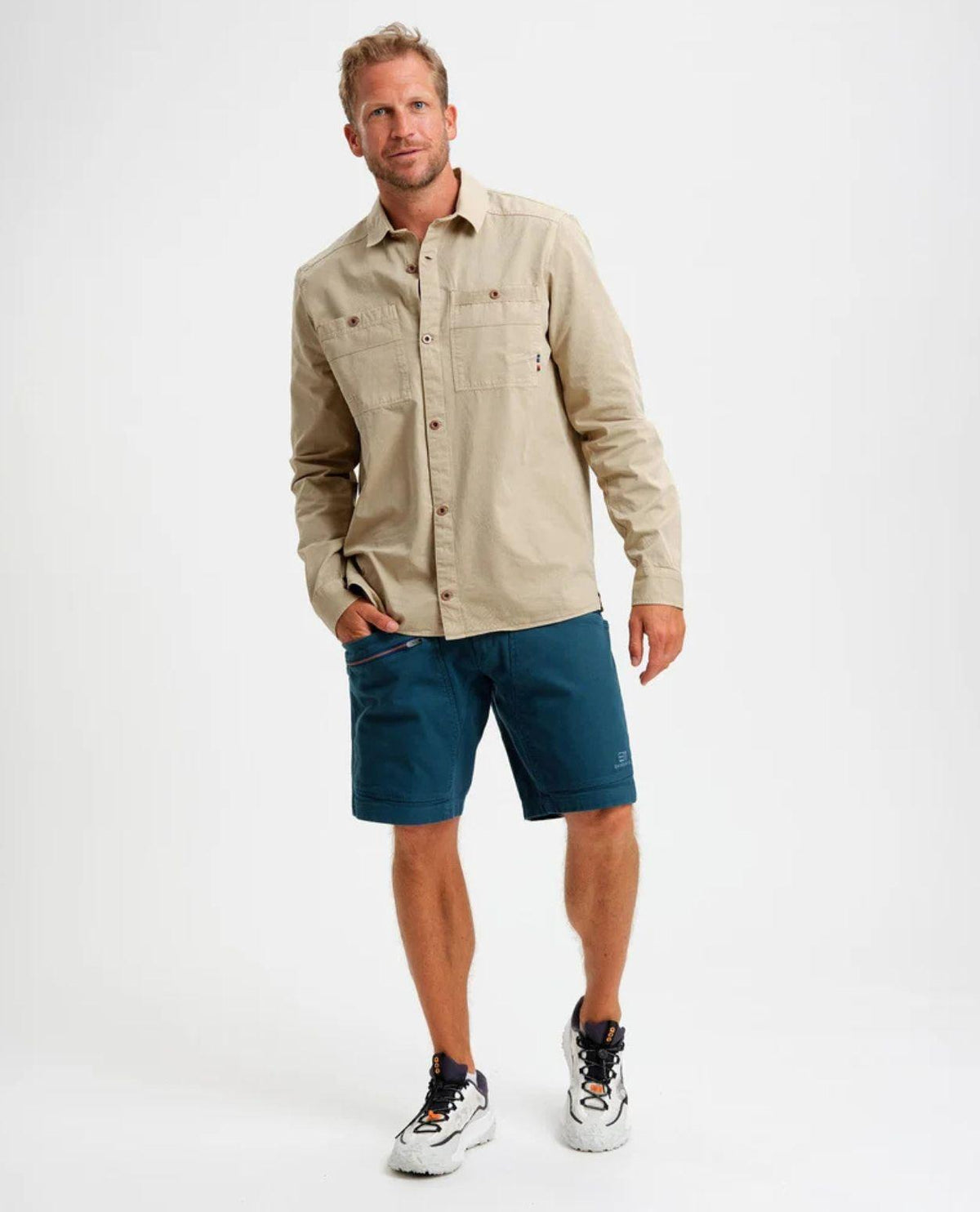 Man i en beige skjorta och blå shorts från Elevenate mot en vit bakgrund.