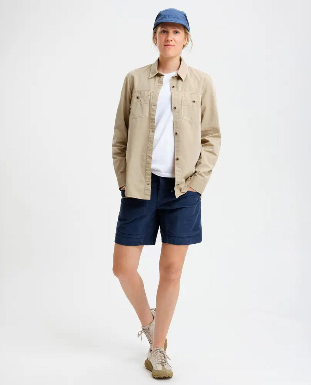 Kvinna som bär Elevenate Utility Shirt i färgen safari beige tillsammans med blå shorts och keps.