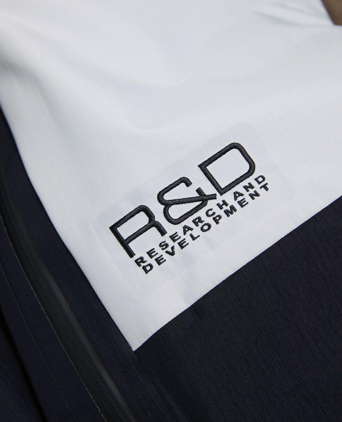Närbild på broderad R&D-logotyp på Peak Performance skidbyxor i modell Vertical Gore-Tex Pro Bib Pants för herrar.