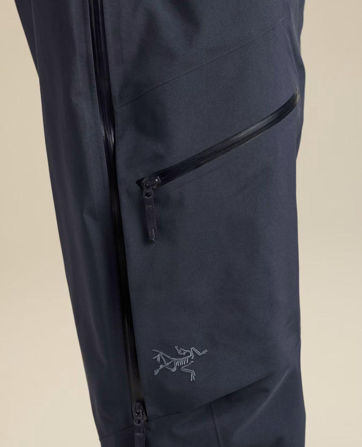 Närbild på Arc'teryx skidbyxor i mörkblått med en snedställd ficka med dragkedja och broderad logotyp på benet.