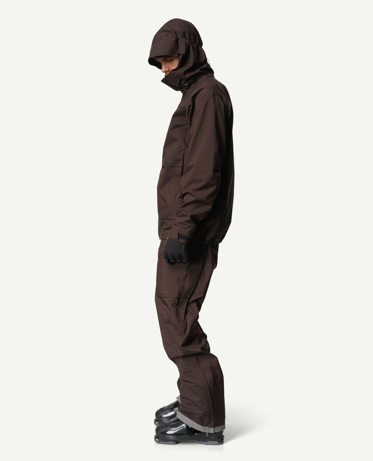 Man i profil som bär den bruna Houdini Rollercoaster Jacket II och matchande skidbyxor med pjäxor.