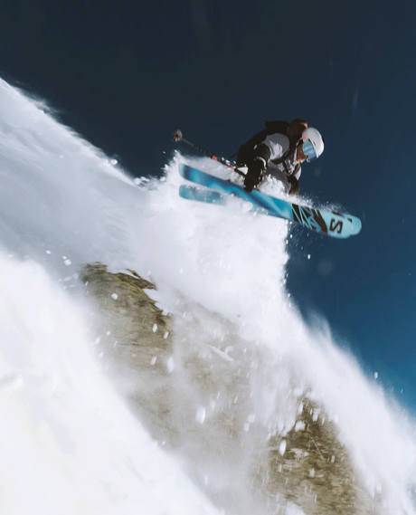 En friåkare hoppar i pudersnö med skidpaketet Salomon QST 100 Cosmic Sky och Strive 12 GW bindningar, ett perfekt val för den äventyrliga skidåkaren över hela berget.