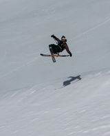 Skidåkare i luften som utför ett hopp med Völkl Revolt 86 parkskidor i ett snöigt bergslandskap.