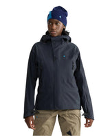 En modell i Klättermusen Svalinn Hood Jacket för dam i svart färg med asymmetrisk dragkedja fram och tillhörande mössa.