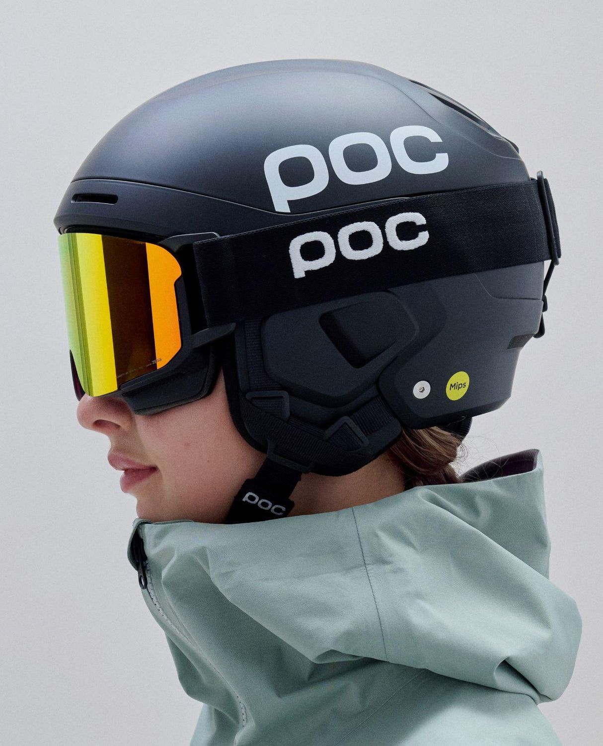 Svart POC Nexal Mid skidglasögon med orange lins buren med hjälm i profil.