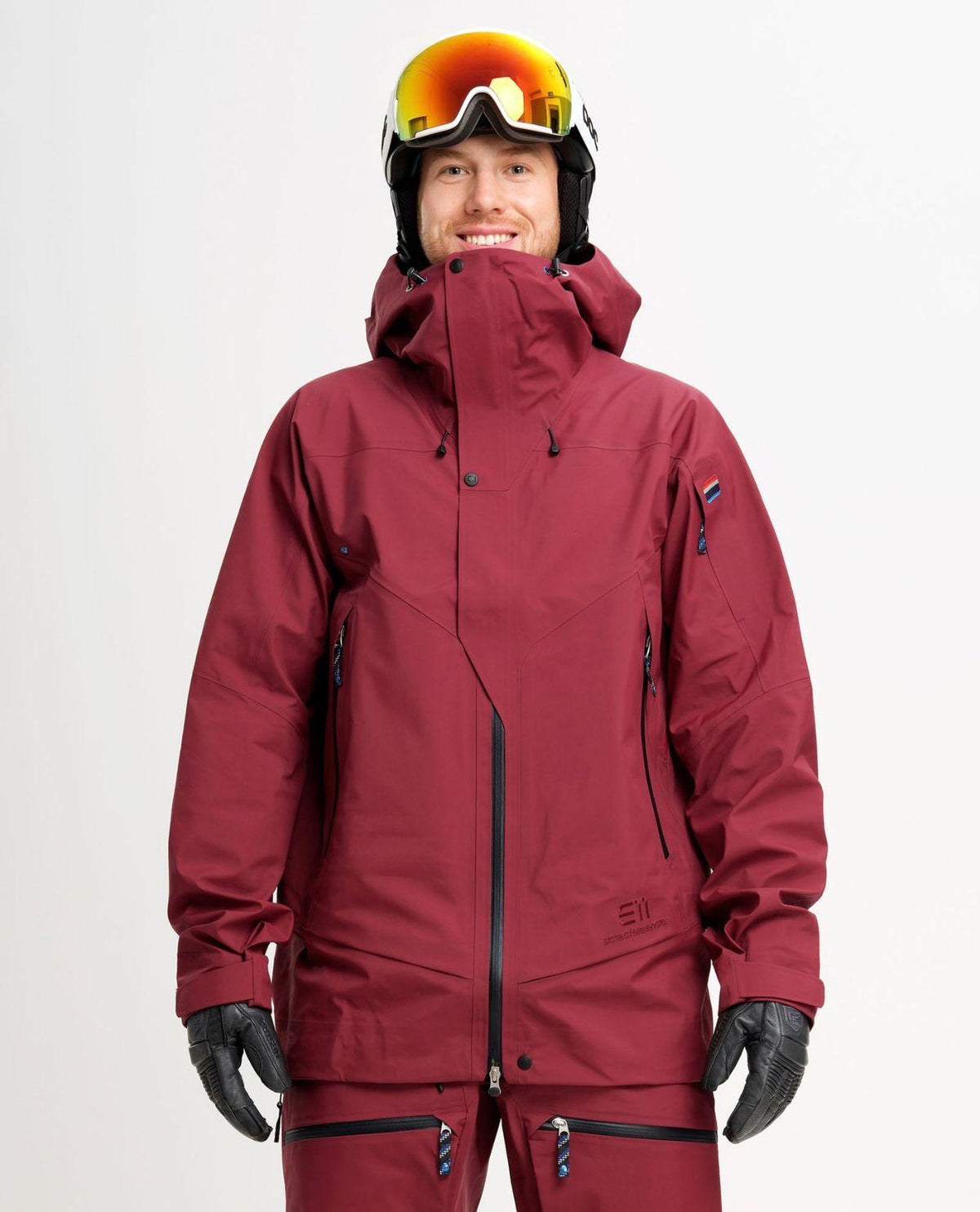 Elevenate Pure Jacket Men i färgen Tibetan Red på en manlig skidåkare iförd hjälm och skidglasögon.