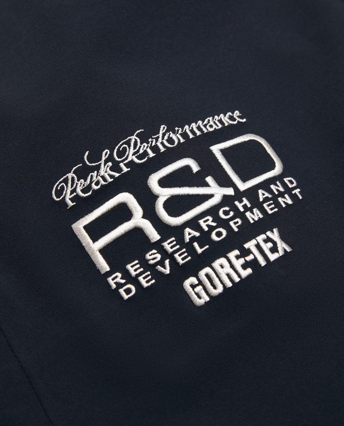 Närbild på vit brodyr med Peak Performance R&D och Gore-Tex-logotyp på svarta skidbyxor.
