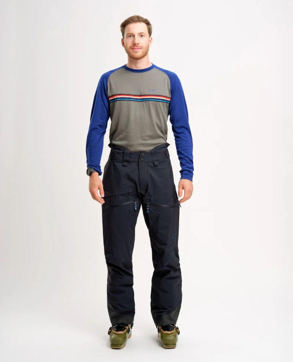 Man som står upp och visar Elevenate Pure Pants Men i mörkblått samt en tröja och pjäxor.