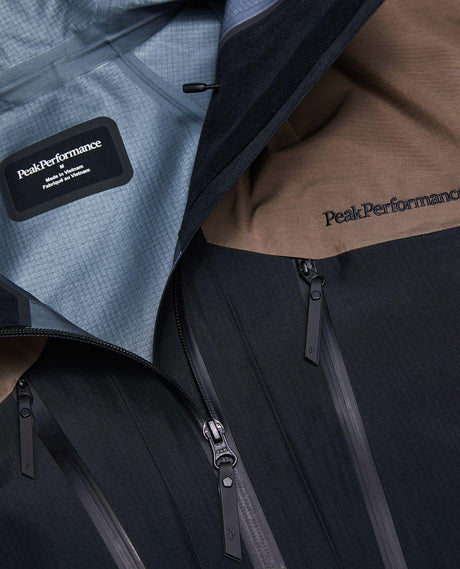 Närbild på Peak Performance Vertical Gore-Tex Pro Jacket Men i offblack och terrain tan som visar detaljer som dragkedjor och logotyp.
