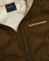 Närbild på Peak Performance Helium Down Hood Jacket Junior i färgerna Meadow Moss och Sand Fog med bröstlogotyp.