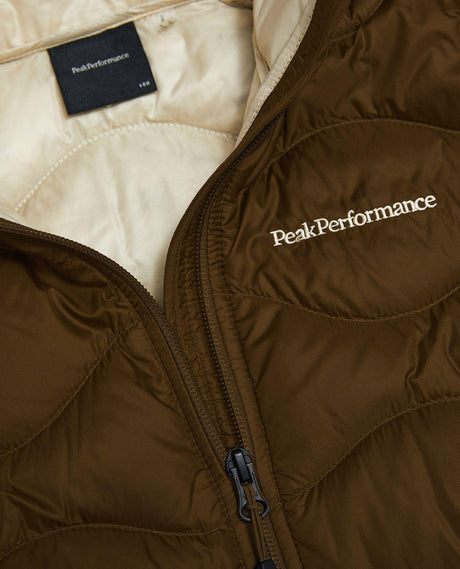 Närbild på Peak Performance Helium Down Hood Jacket Junior i färgerna Meadow Moss och Sand Fog med bröstlogotyp.