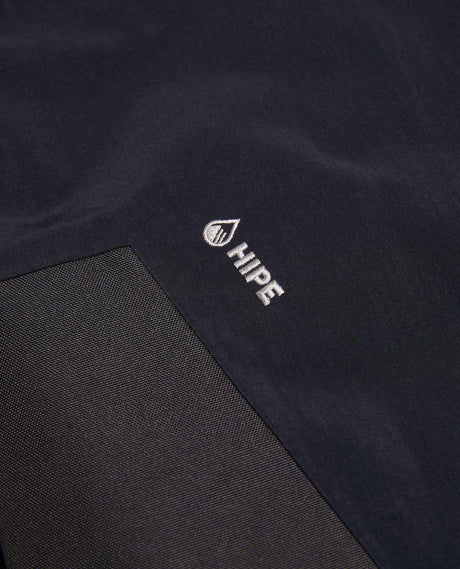 Närbild på det svarta HIPE-materialet och logotypen på Peak Performance Edge 3L Bib Pants Women.