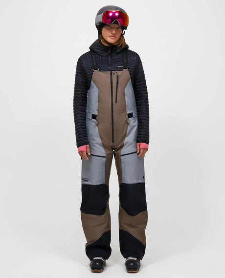 Skidåkare i dammodellens Peak Performance Vertical Gore-Tex Pro Bib Pants i färgen Terrain Tan och ljusgrå framifrån.