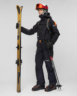Skidåkare i svart Mammut Eiger Free Pro HS Hooded Jacket med matchande byxor, skidglasögon och skidor.