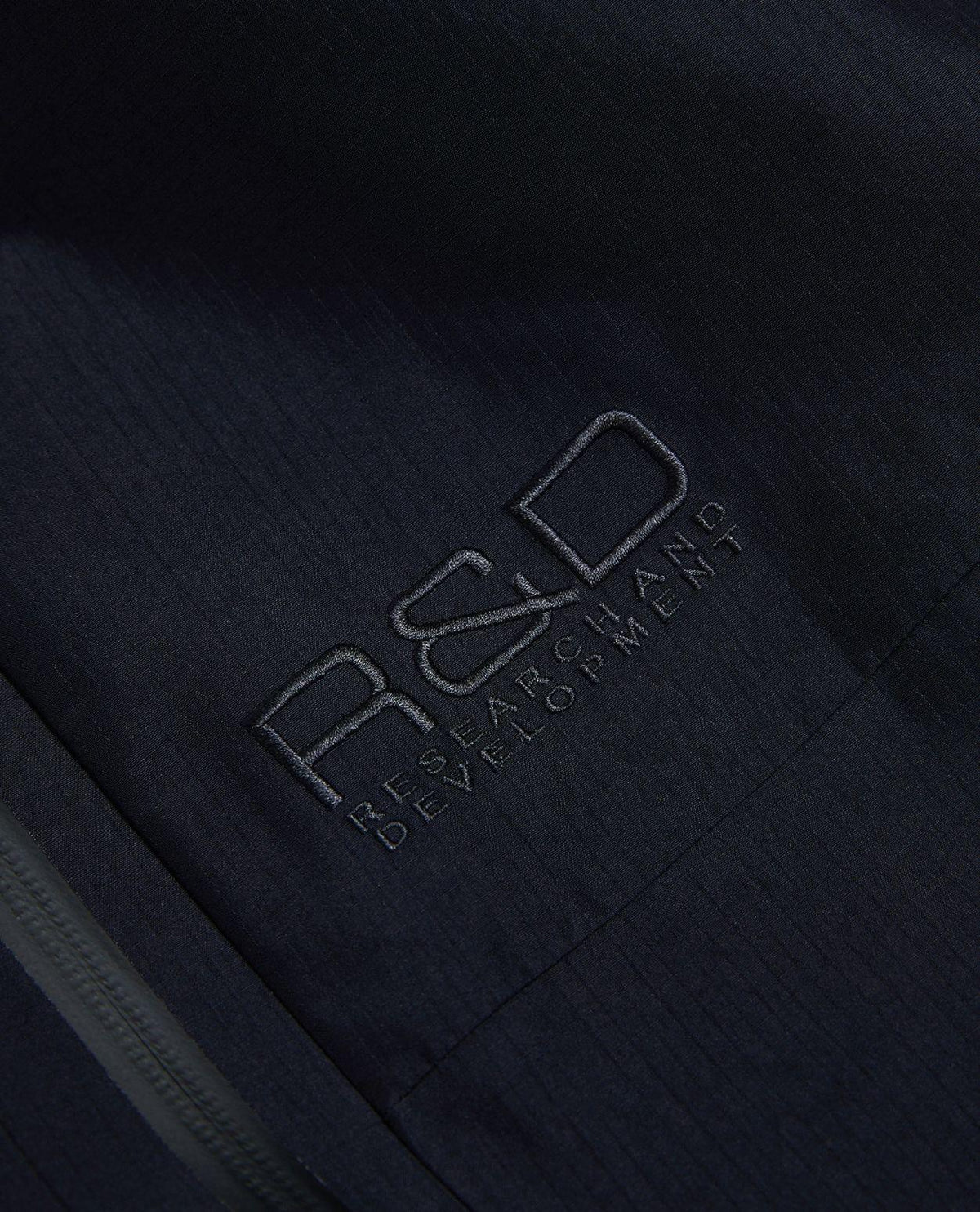 Detaljbild på broderad R&D-logotyp på svarta skidbyxor från Peak Performance.