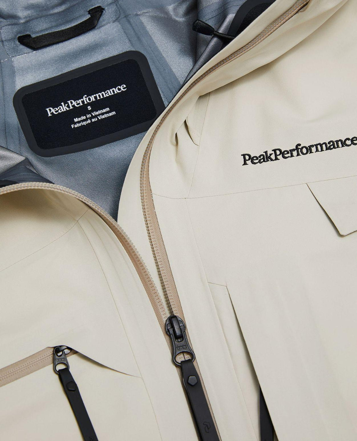 Närbild på innerfoder, logotyp och dragkedjor på Peak Performance Alpine Gore-Tex 3L Jacket Dam i färgen Sand Fog.