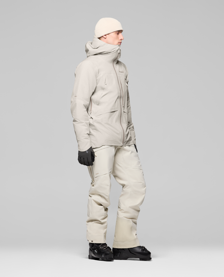 Norrøna Møre Gore-Tex Jacket Men i färgen Oatmeal, visad från sidan med matchande skidbyxor och pjäxor för herrar.