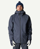 Manlig skidåkare iförd en blå Houdini Ride Jacket II och matchande mössa, utrustad med skidhandskar.