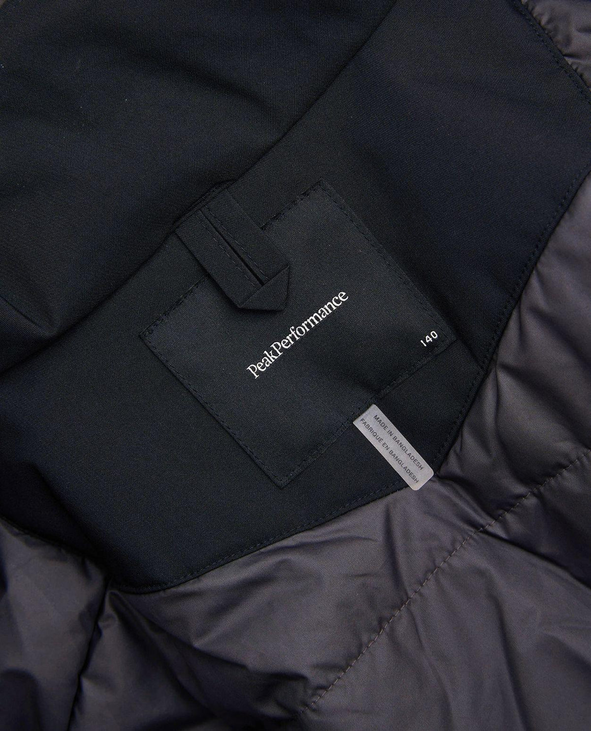 Detaljbild på innerfoder och logotyp i nackan på Peak Performance Gravity Insulated Jacket Junior i svart.