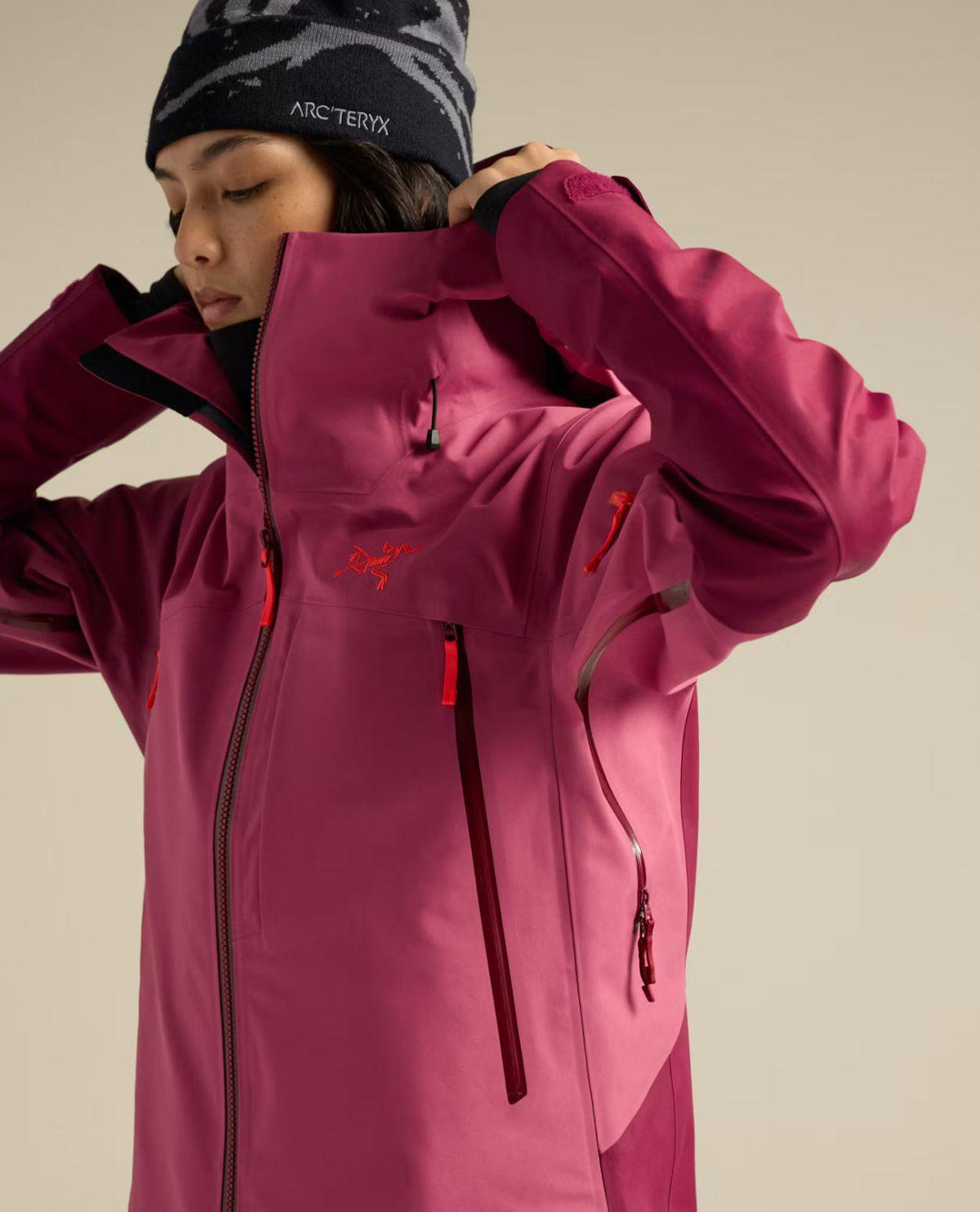 Kvinna i profil som bär en rosa skidjacka från Arc'teryx med hög krage och dragkedja, iklädd en svart mössa.