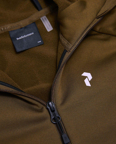 Peak Performance Rider Essentials Zip Hood Junior i grön Meadow Moss visar bröstdetaljer och logotyp.
