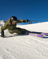 Skidåkare i grön jacka skär en sväng i pisten på Armada ANTIMATTER 100 Women allmountainskidor under solig dag.