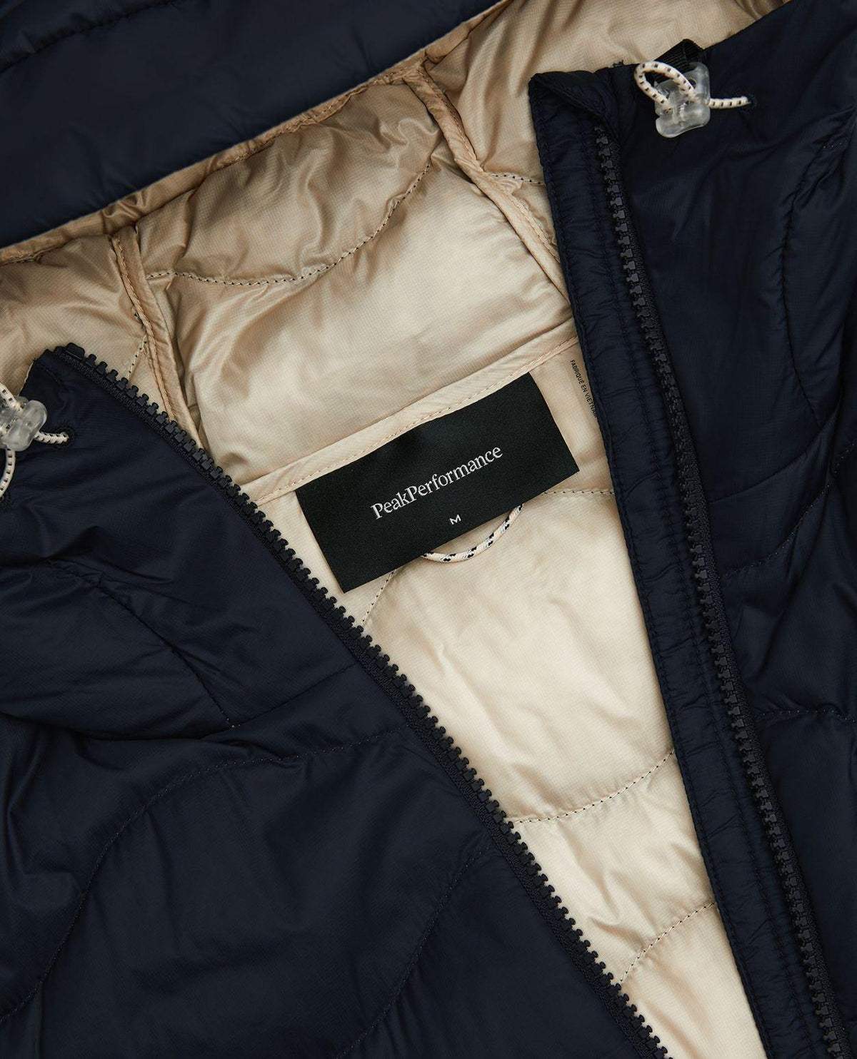 Peak Performance Helium Utility Down Hood Jacket i svart med sandfärgat foder och inneretikett med logotyp.