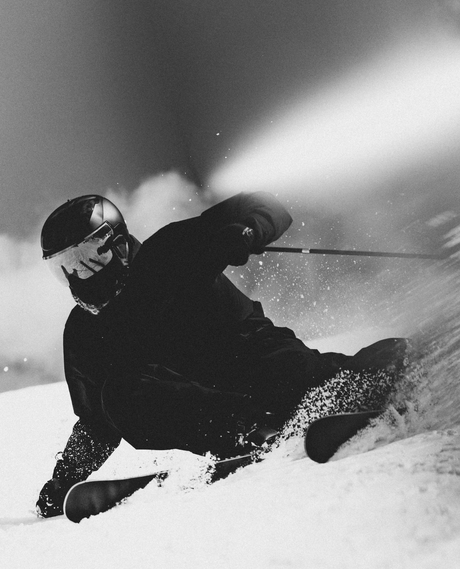 Alpin skidåkare som lägger sina Atomic Volant 9000 på kant i en kraftfull sväng med dramatiskt snöstänk.