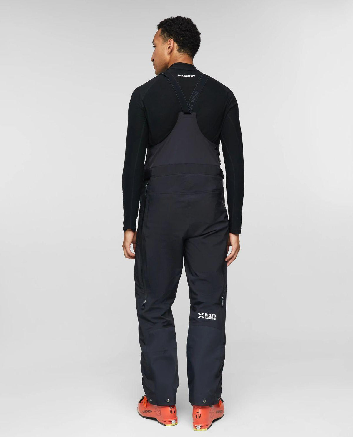 Man bakifrån iförd svarta Mammut Eiger Free Pro HS hängselbyxor och orange pjäxor.