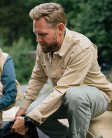 En man iklädd Elevenate Utility Shirt Men i safari beige huka sig ned utomhus.