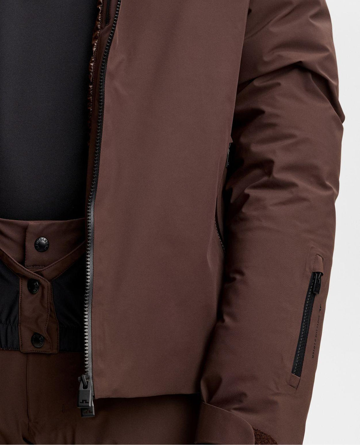 Närbild på J.Lindeberg Oak Down Jacket i färgen Seal Brown med detaljer som dragkedja och ärmficka.