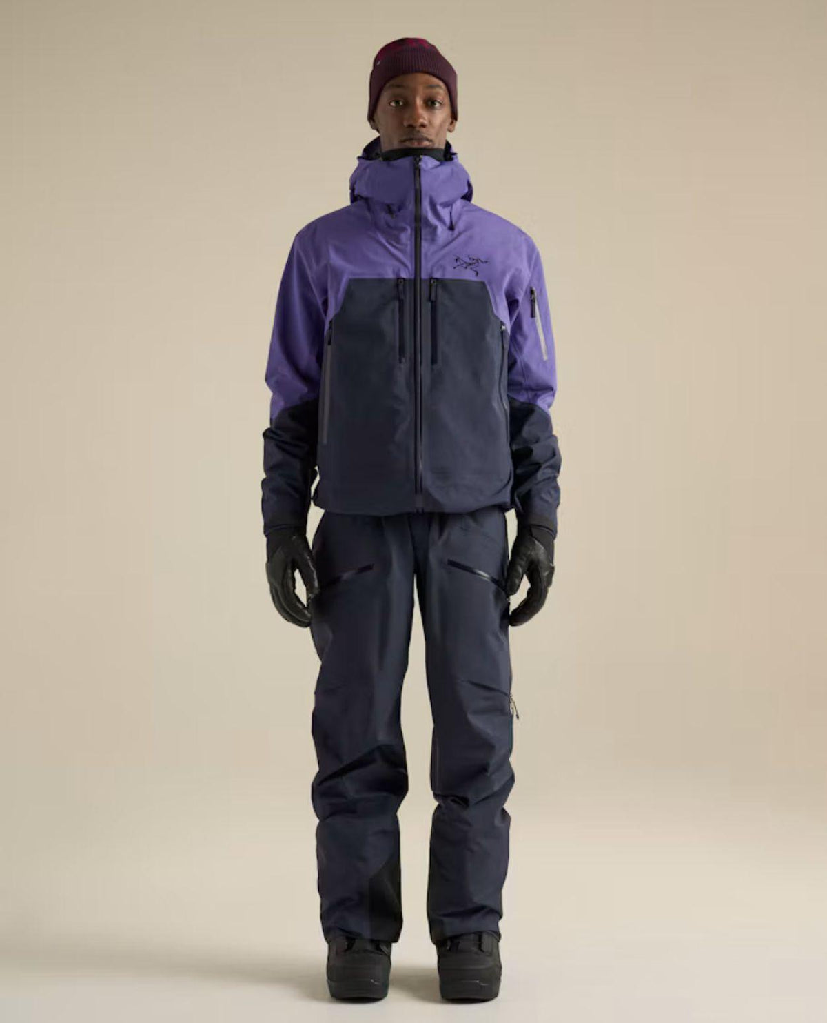Person bär en lila och mörkblå skidjacka av märket Arc'teryx Rush Jacket Men tillsammans med matchande skidbyxor och mössa.
