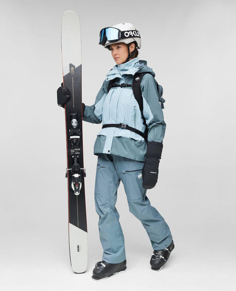 Mammut Haldigrat Gore-Tex HS Thermo Hooded Jacket Women i Nebla-Strata färg, visad med skidutrustning och skidor.