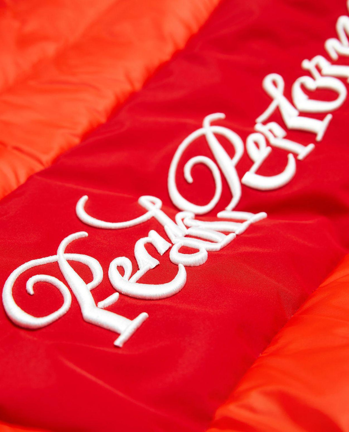 Närbild på den vita broderade Peak Performance-logotypen på den röda dunjackan för herrar.
