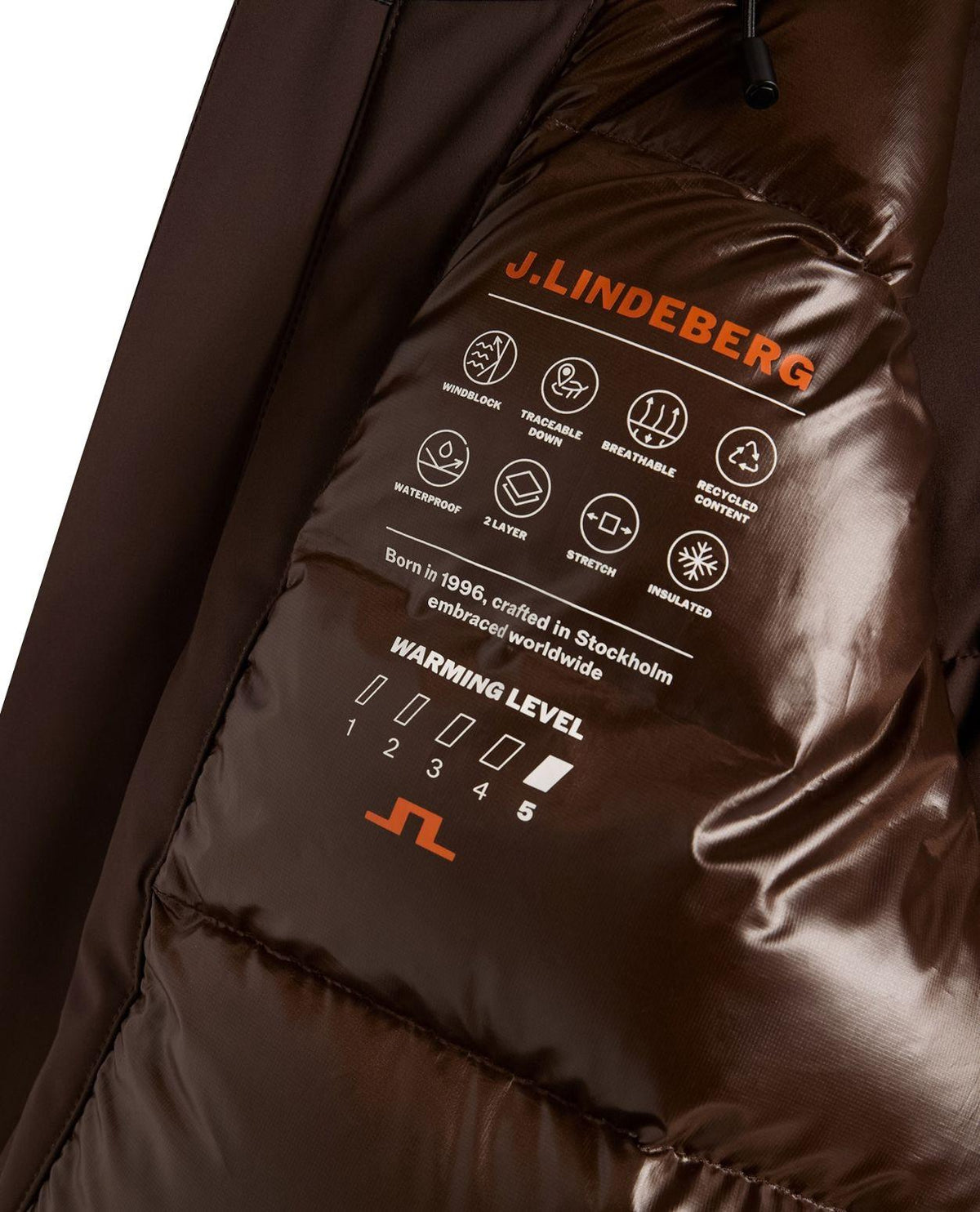 Närbild på innerfoder med funktionsikoner och warming level i J.Lindeberg Oak Down Jacket för herrar i färgen brun.