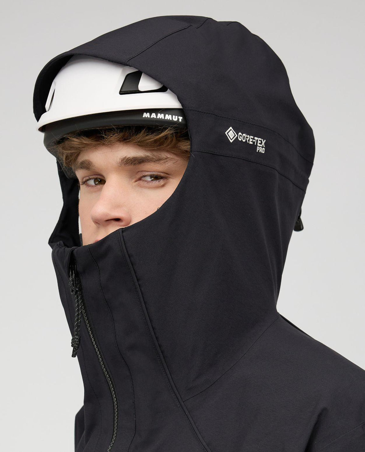 Skidåkare i svart Mammut Eiger Free Pro HS Hooded Jacket med hjälm och huva uppdragen.
